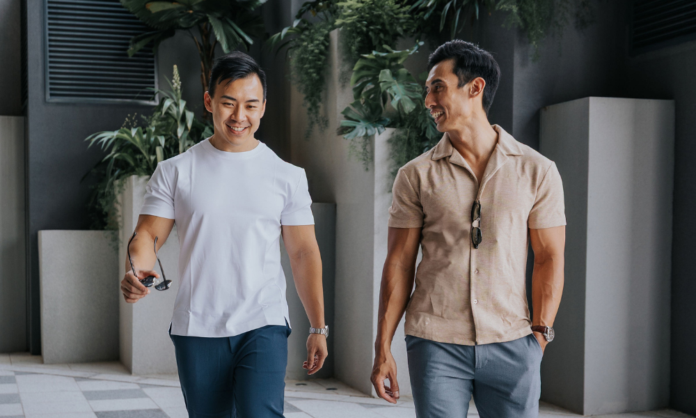 Two men walking together in an indoor setting with plants in the background wearing clothes for men 175cm & under