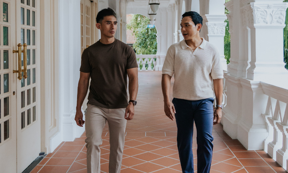 Two men walking in a hallway with white walls and a tiled floor wearing a shirt and t-shirt for short men. Luxury knit polo and tailored tee for men 175cm & under