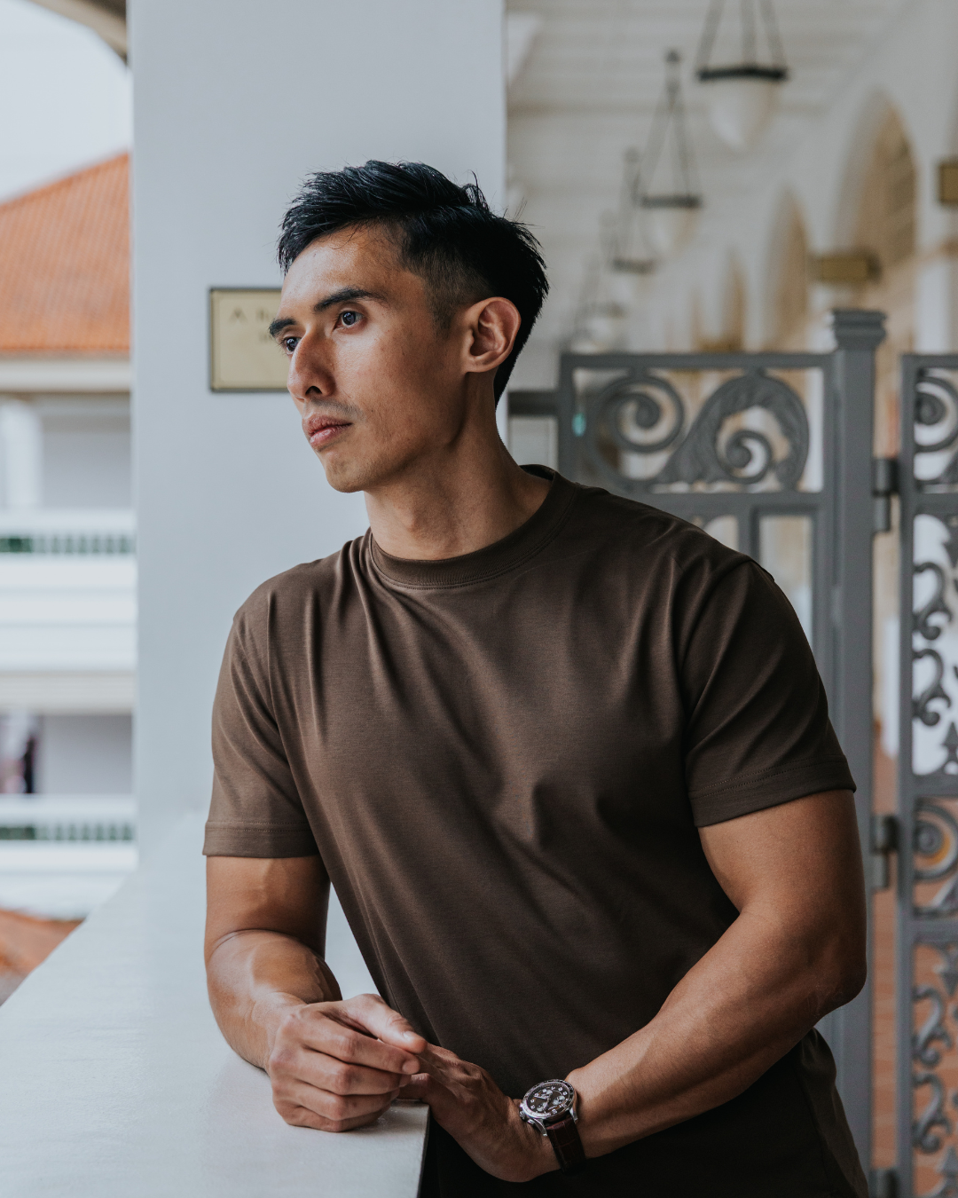 Man wearing a brown t-shirt standing indoors with a blurred background - essentials for short men