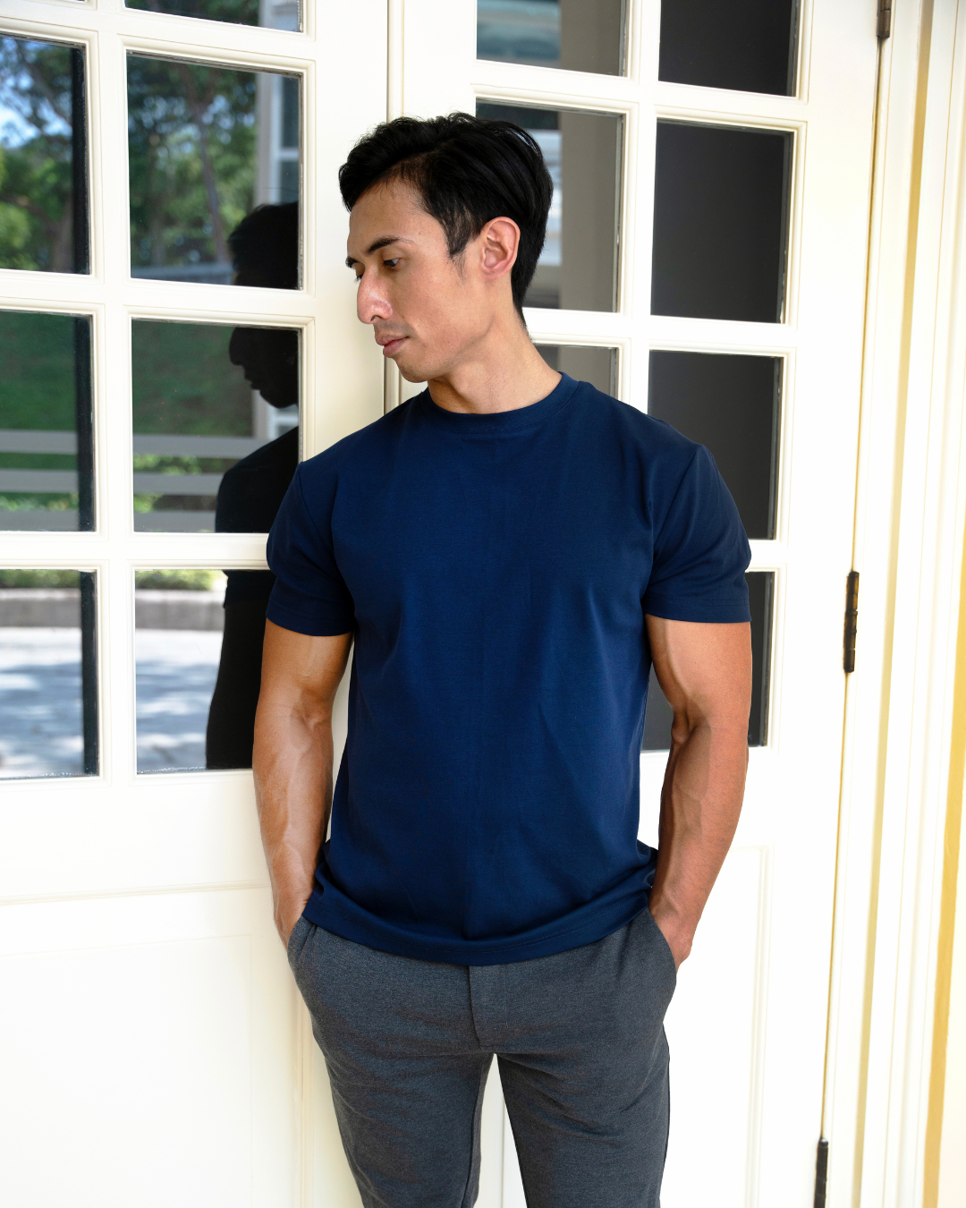 Man wearing a navy blue t-shirt and gray pants standing in front of a window showcasing men’s clothing for short men