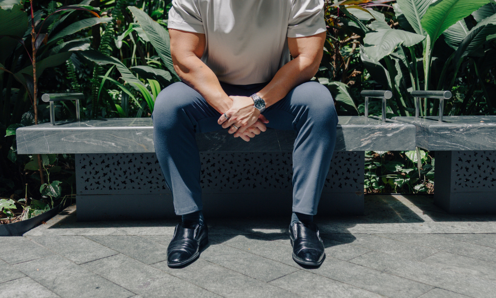 Person sitting on a bench with greenery in the background wearing a business casual performance pants for short men