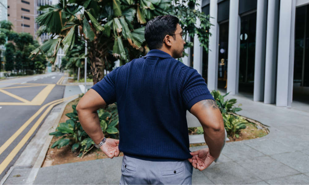 Man in a blue shirt standing on a city street with plants and buildings in the background wearing shirts for men 175cm & under
