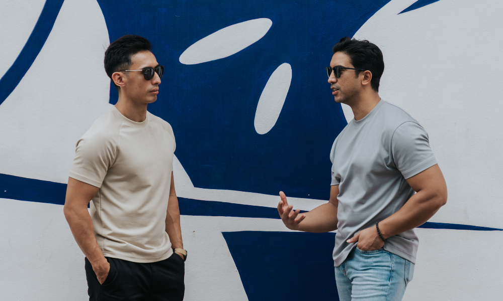 Two men standing in front of a blue and white logo wearing clothing for short men. Tailored t-shirt and raglan t-shirt