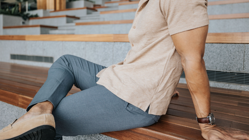 Person sitting on a wooden bench wearing a beige shirt and blue pants wear trousers for short men.